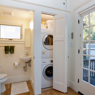 Photo of a small traditional single-wall laundry cupboard in San Francisco with a single-bowl sink, shaker cabinets, medium hardwood flooring, a stacked washer and dryer, white cabinets, white walls and brown floors.