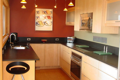 Example of a minimalist u-shaped enclosed kitchen design in Seattle with a double-bowl sink, flat-panel cabinets, light wood cabinets, black backsplash and stainless steel appliances