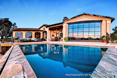 Photo of a large mediterranean backyard patio in San Diego with an outdoor kitchen, natural stone pavers and a roof extension.