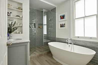 Photo of a beach style 3/4 bathroom in London with grey cabinets, a freestanding tub, gray tile, white walls, an undermount sink, a hinged shower door, an alcove shower, beige floor and grey benchtops.
