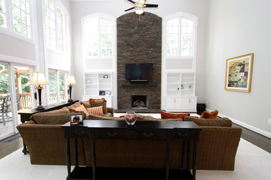 Example of a large trendy dark wood floor living room design in Los Angeles with white walls, a standard fireplace, a stone fireplace and a wall-mounted tv