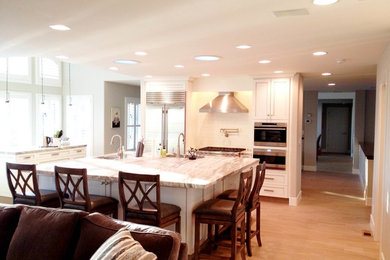 Example of a mid-sized trendy l-shaped light wood floor open concept kitchen design in Other with a double-bowl sink, shaker cabinets, white cabinets, white backsplash, subway tile backsplash, stainless steel appliances and an island