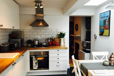 Inspiration for a medium sized farmhouse l-shaped kitchen/diner in Hertfordshire with a single-bowl sink, flat-panel cabinets, white cabinets, wood worktops, white splashback, ceramic splashback, stainless steel appliances, ceramic flooring, no island and black floors.