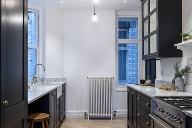Inspiration for a medium sized rural galley kitchen in London with shaker cabinets, marble worktops, stainless steel appliances, a belfast sink, black cabinets, light hardwood flooring, no island, beige floors and white worktops.