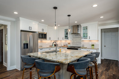 Example of a mid-sized transitional l-shaped medium tone wood floor and brown floor kitchen design in Other with an undermount sink, recessed-panel cabinets, white cabinets, white backsplash, stainless steel appliances, an island and multicolored countertops