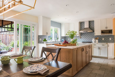 Mid-sized transitional u-shaped porcelain tile and gray floor eat-in kitchen photo in San Francisco with a farmhouse sink, shaker cabinets, white cabinets, quartz countertops, blue backsplash, glass tile backsplash, stainless steel appliances, an island and multicolored countertops