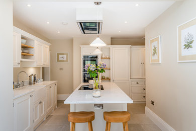 Photo of a medium sized classic l-shaped open plan kitchen in London with a belfast sink, shaker cabinets, beige cabinets, composite countertops, black appliances, porcelain flooring, an island, grey floors and white worktops.