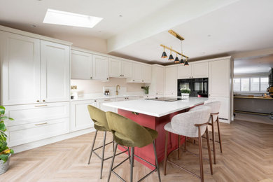 Design ideas for a large l-shaped kitchen/diner in Other with a submerged sink, shaker cabinets, beige cabinets, quartz worktops, white splashback, black appliances, medium hardwood flooring, an island, brown floors and white worktops.