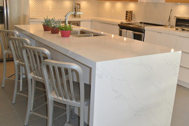 Inspiration for a mid-sized modern porcelain tile eat-in kitchen remodel in Other with a drop-in sink, flat-panel cabinets, white cabinets, quartz countertops, white backsplash, glass sheet backsplash, stainless steel appliances and an island