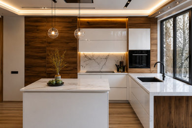 Medium sized contemporary grey and brown l-shaped open plan kitchen in Oxfordshire with a submerged sink, flat-panel cabinets, white cabinets, composite countertops, white splashback, engineered quartz splashback, black appliances, medium hardwood flooring, an island, brown floors, white worktops, a coffered ceiling and feature lighting.