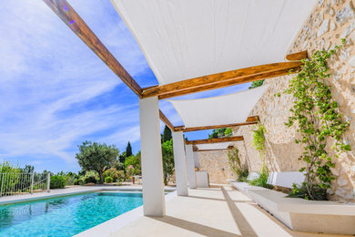 Réalisation d'un jardin avec pergola avant méditerranéen avec une exposition ensoleillée et des pavés en pierre naturelle.