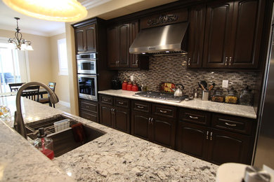 Example of a large minimalist galley travertine floor open concept kitchen design in Orange County with an undermount sink, raised-panel cabinets, dark wood cabinets, granite countertops, metallic backsplash, glass sheet backsplash, stainless steel appliances and an island