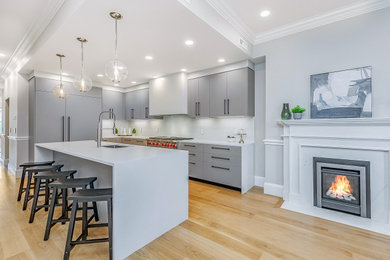 Mid-sized trendy l-shaped light wood floor, beige floor and tray ceiling eat-in kitchen photo in Boston with an undermount sink, flat-panel cabinets, beige cabinets, quartz countertops, white backsplash, stainless steel appliances, an island and white countertops