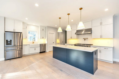 Inspiration for a large transitional l-shaped light wood floor and beige floor open concept kitchen remodel in Boston with a farmhouse sink, shaker cabinets, white cabinets, quartz countertops, white backsplash, ceramic backsplash, stainless steel appliances, an island and white countertops