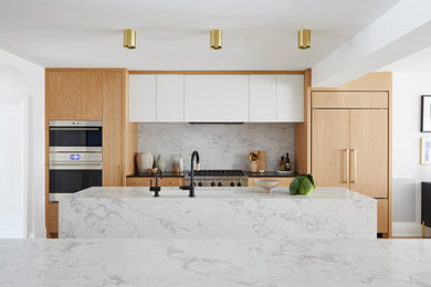 Inspiration for a large contemporary galley light wood floor and brown floor open concept kitchen remodel in Toronto with an undermount sink, flat-panel cabinets, light wood cabinets, marble countertops, white backsplash, stone slab backsplash, paneled appliances, two islands and white countertops