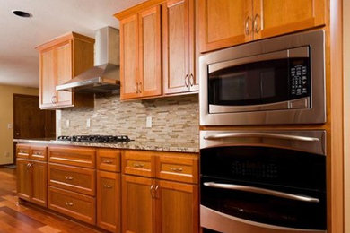 Example of a transitional medium tone wood floor kitchen design in Calgary with shaker cabinets, medium tone wood cabinets, granite countertops, beige backsplash, matchstick tile backsplash and stainless steel appliances