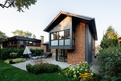 Aménagement d'une petite façade de maison orange rétro en brique et bardeaux à un étage avec un toit à deux pans, un toit en shingle et un toit noir.