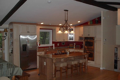 Example of a large classic l-shaped medium tone wood floor eat-in kitchen design in Other with an undermount sink, raised-panel cabinets, beige cabinets, granite countertops, red backsplash, stainless steel appliances and an island