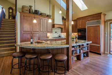Inspiration for a mid-sized timeless single-wall medium tone wood floor eat-in kitchen remodel in Denver with an undermount sink, raised-panel cabinets, medium tone wood cabinets, granite countertops, blue backsplash, stone tile backsplash, paneled appliances and an island