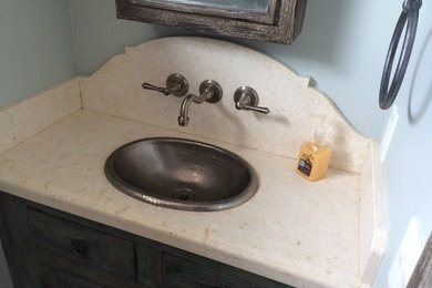 Example of a small mountain style beige tile powder room design in San Diego with a drop-in sink, furniture-like cabinets, distressed cabinets, limestone countertops and a one-piece toilet