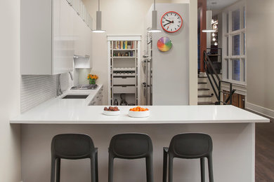 Example of a mid-sized trendy l-shaped dark wood floor and gray floor kitchen design in Chicago with an undermount sink, flat-panel cabinets, white cabinets, quartz countertops, gray backsplash, glass tile backsplash, stainless steel appliances and a peninsula