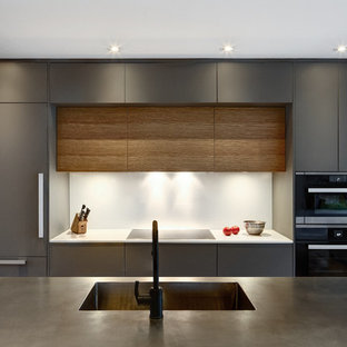 Новые идеи обустройства дома: маленькая параллельная кухня в стиле модернизм с обеденным столом, монолитной раковиной, плоскими фасадами, серыми фасадами, столешницей из нержавеющей стали, фартуком с окном, черной техникой, светлым паркетным полом и островом