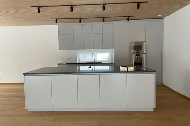 Idéer för ett mellanstort modernt grå kök, med en undermonterad diskho, släta luckor, grå skåp, granitbänkskiva, vitt stänkskydd, fönster som stänkskydd, rostfria vitvaror, ljust trägolv och en köksö