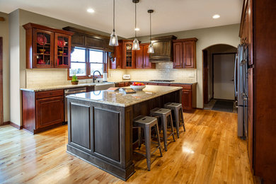 Mid-sized traditional u-shaped open plan kitchen in Minneapolis with a farmhouse sink, raised-panel cabinets, dark wood cabinets, granite benchtops, white splashback, ceramic splashback, stainless steel appliances, light hardwood floors, with island, yellow floor and white benchtop.