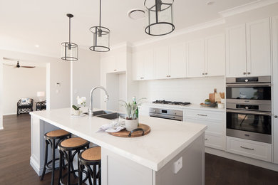 This is an example of a mid-sized traditional galley eat-in kitchen in Sydney with a double-bowl sink, shaker cabinets, grey cabinets, solid surface benchtops, white splashback, ceramic splashback, stainless steel appliances, dark hardwood floors, with island, brown floor and white benchtop.