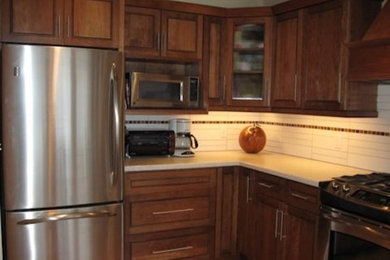 Eat-in kitchen - mid-sized traditional l-shaped eat-in kitchen idea in Calgary with raised-panel cabinets, medium tone wood cabinets, solid surface countertops, white backsplash, ceramic backsplash and stainless steel appliances