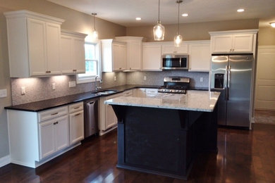 Large trendy l-shaped dark wood floor and brown floor open concept kitchen photo in Cleveland with an undermount sink, shaker cabinets, white cabinets, granite countertops, beige backsplash, stone tile backsplash, stainless steel appliances and an island