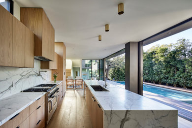 Inspiration for a large modern single-wall light wood floor and beige floor open concept kitchen remodel in Los Angeles with an undermount sink, flat-panel cabinets, light wood cabinets, marble countertops, white backsplash, marble backsplash, stainless steel appliances, an island and white countertops
