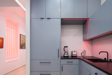 Design ideas for a mid-sized contemporary l-shaped eat-in kitchen in New York with an undermount sink, flat-panel cabinets, blue cabinets, solid surface benchtops, black splashback, glass sheet splashback, coloured appliances, light hardwood floors, no island and beige floor.