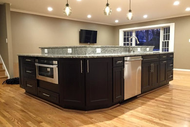 Large transitional galley light wood floor open concept kitchen photo in DC Metro with an undermount sink, recessed-panel cabinets, white cabinets, granite countertops, beige backsplash, white appliances and an island