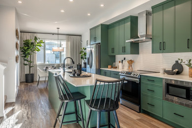 Transitional galley medium tone wood floor and brown floor kitchen photo in Calgary with an undermount sink, recessed-panel cabinets, green cabinets, white backsplash, stainless steel appliances, an island and white countertops