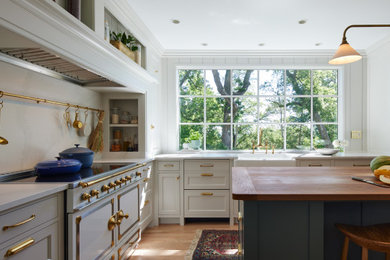 Example of a classic medium tone wood floor enclosed kitchen design in Minneapolis with a farmhouse sink, recessed-panel cabinets, wood countertops, white appliances and an island