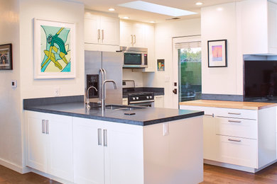 Mid-sized trendy l-shaped light wood floor and brown floor eat-in kitchen photo in Other with an undermount sink, shaker cabinets, white cabinets, granite countertops, black backsplash, stone slab backsplash, stainless steel appliances and black countertops