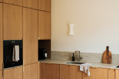 Aménagement d'une cuisine ouverte contemporaine en L et bois brun de taille moyenne avec un placard avec porte à panneau encastré, un plan de travail en quartz, une crédence beige, une crédence en quartz modifié, un électroménager noir, un sol en bois brun, îlot et un plan de travail beige.