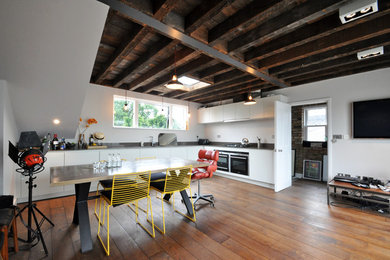 Photo of a medium sized industrial l-shaped open plan kitchen in London with flat-panel cabinets, white cabinets, medium hardwood flooring, no island, a built-in sink, stainless steel worktops and stainless steel appliances.