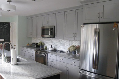 Large trendy single-wall light wood floor eat-in kitchen photo in New York with an undermount sink, shaker cabinets, gray cabinets, quartz countertops, white backsplash, stone tile backsplash, stainless steel appliances and an island
