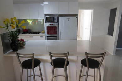 Photo of a mid-sized modern galley separate kitchen in Melbourne with a drop-in sink, flat-panel cabinets, white cabinets, quartz benchtops, green splashback, glass sheet splashback, stainless steel appliances, porcelain floors and with island.