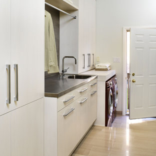 Contemporary utility room in Toronto with stainless steel worktops, limestone flooring, a side by side washer and dryer, beige floors, white cabinets, an integrated sink and white walls.