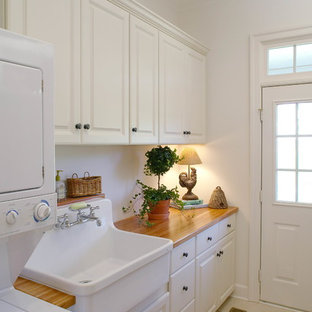 Design ideas for a small classic utility room in DC Metro with raised-panel cabinets, white cabinets, wood worktops, white walls, a stacked washer and dryer, travertine flooring, beige worktops and a belfast sink.