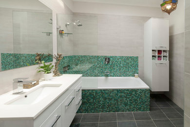 Photo of a mid-sized contemporary bathroom in Canberra - Queanbeyan with an undermount sink, flat-panel cabinets, white cabinets, engineered quartz benchtops, a drop-in tub, a shower/bathtub combo, a one-piece toilet, multi-coloured tile, mosaic tile and ceramic floors.