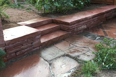 Photo of a small eclectic backyard full sun garden in Denver with a retaining wall and natural stone pavers.