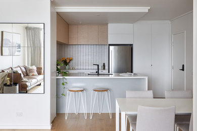 Inspiration for a small contemporary u-shaped open plan kitchen in Melbourne with an undermount sink, flat-panel cabinets, white cabinets, quartzite benchtops, white splashback, ceramic splashback, stainless steel appliances, light hardwood floors, with island and white benchtop.