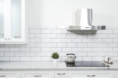 Inspiration for a mid-sized contemporary kitchen remodel in Boston with glass-front cabinets, white cabinets, quartz countertops, white backsplash, subway tile backsplash, stainless steel appliances and gray countertops