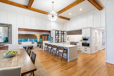 Inspiration for a mid-sized transitional u-shaped medium tone wood floor, brown floor and shiplap ceiling eat-in kitchen remodel in Charlotte with a farmhouse sink, shaker cabinets, white cabinets, quartzite countertops, beige backsplash, stone slab backsplash, stainless steel appliances, a peninsula and beige countertops