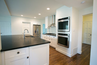 Eat-in kitchen - large modern single-wall medium tone wood floor eat-in kitchen idea in Other with an undermount sink, shaker cabinets, white cabinets, solid surface countertops, black backsplash, stainless steel appliances and an island