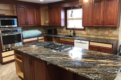Example of a minimalist l-shaped kitchen design in New York with raised-panel cabinets, brown cabinets, marble countertops, beige backsplash, ceramic backsplash and stainless steel appliances